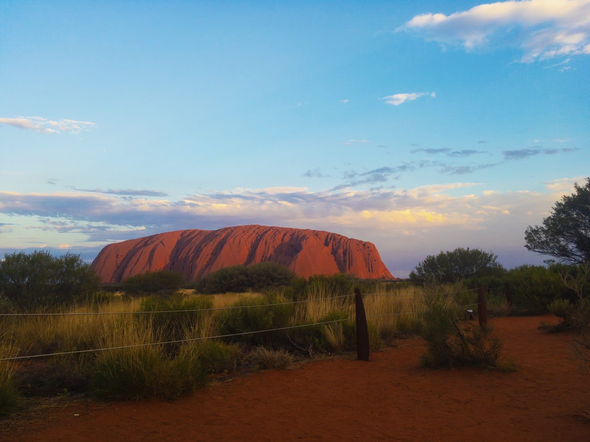 Uluru at dusk — red sandstone and spinifex country against a pale evening sky